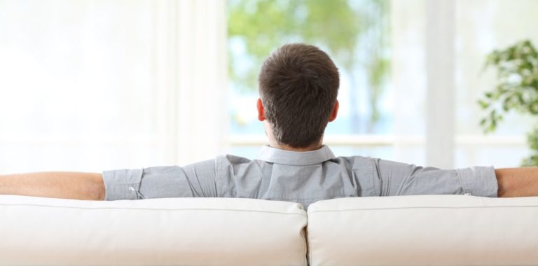 Rear view of a man relaxing sitting on a sofa at home and looking outdoors through the window at home